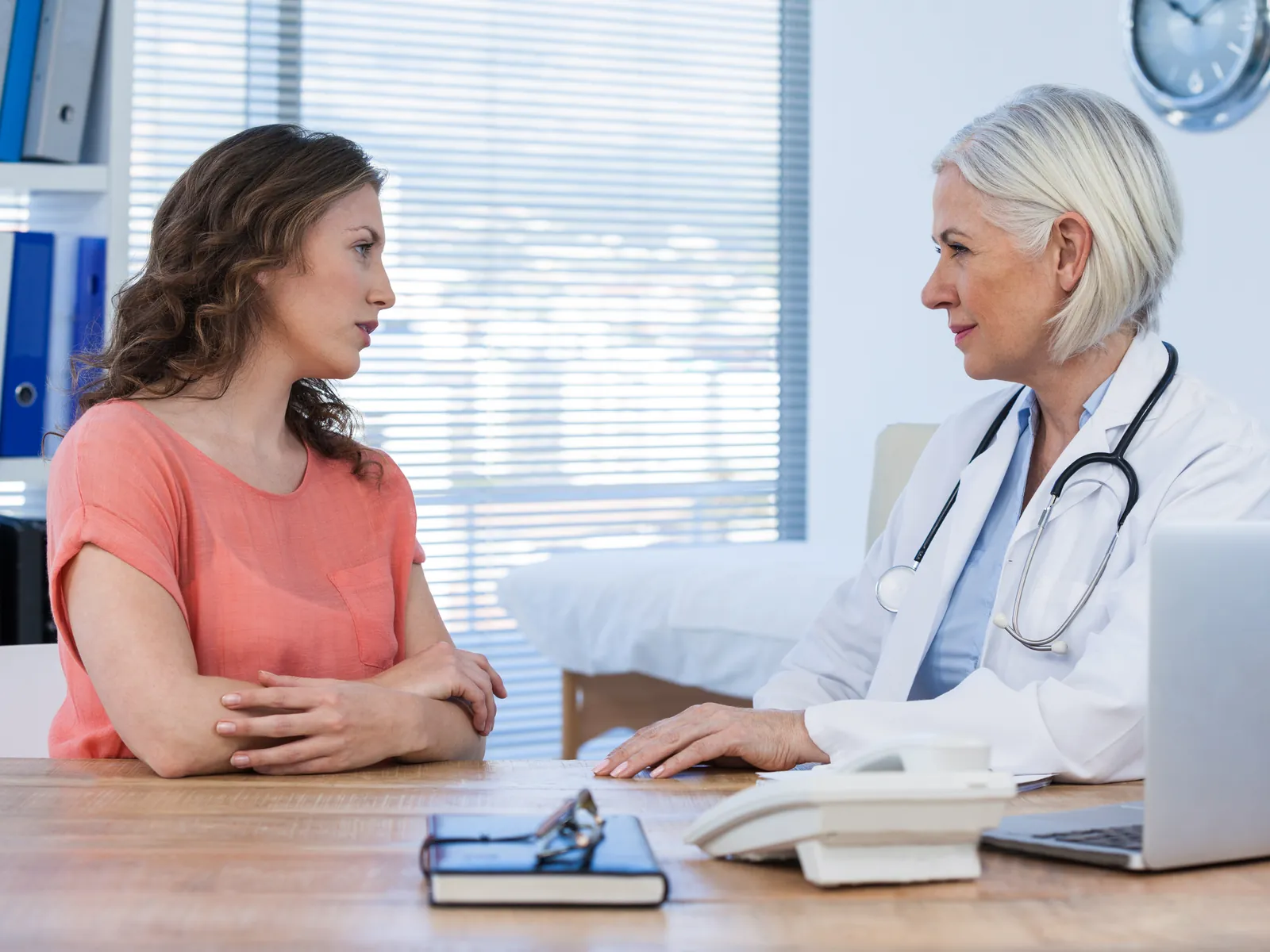 Médica conversa com a paciente sentada à mesa do consultório